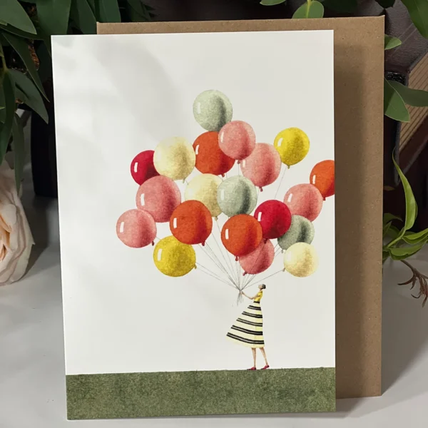 Greeting card showing a person in a striped dress holding a large bunch of colorful balloons, set against a white background with a green base.