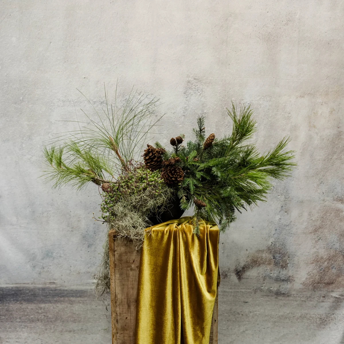 A rustic winter arrangement with pine boughs, pinecones, moss, and heather accents, ideal for seasonal or holiday décor.