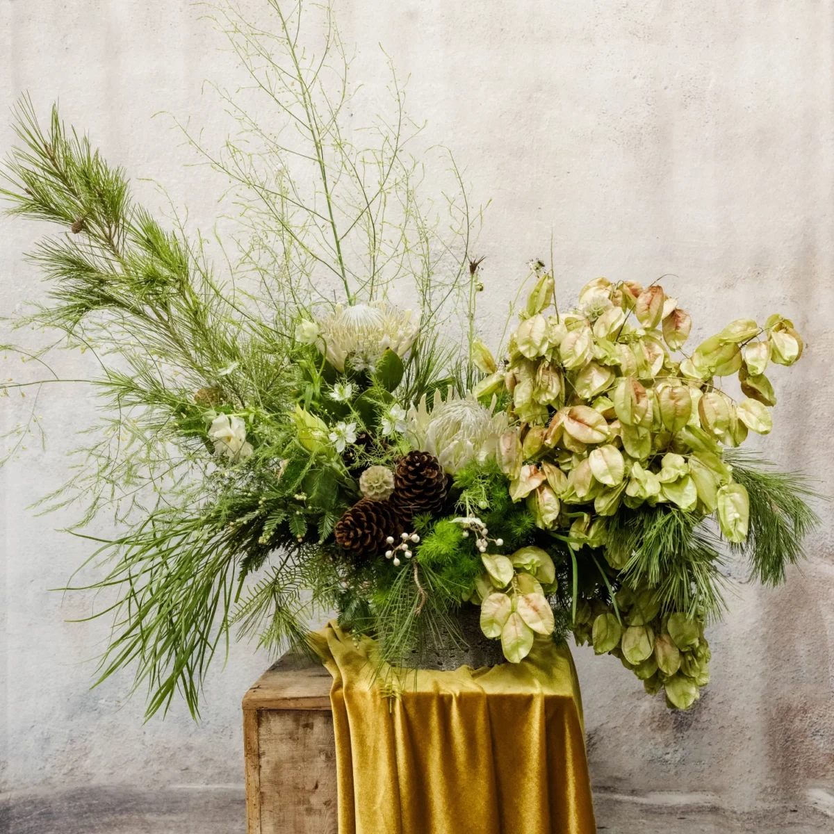 A woodland-inspired arrangement featuring green foliage, cascading amaranthus, white blooms, and pinecones, perfect for seasonal or holiday décor.