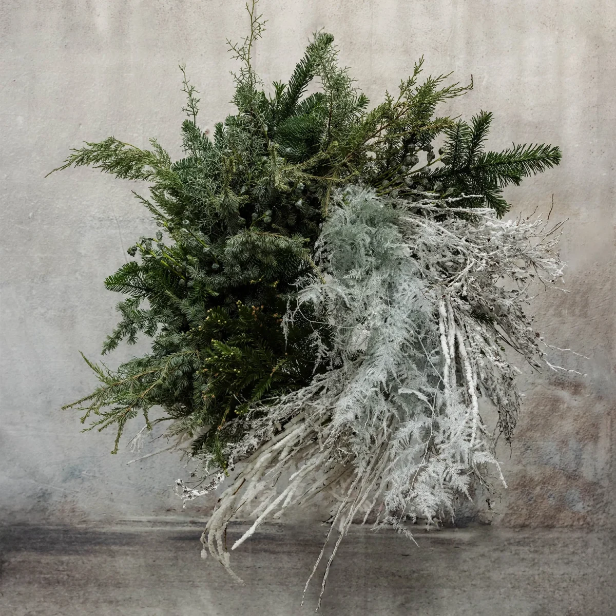 An asymmetrical winter wreath with lush evergreen branches and frosted foliage, ideal for holiday or seasonal décor.