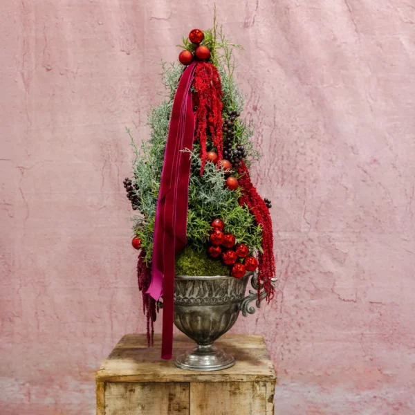 Holiday topiary featuring red berries, cascading crimson ribbons, evergreen accents, and a silver urn, designed as part of the Crimson Euphoria Collection.