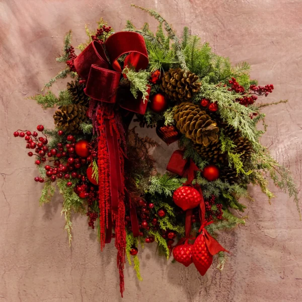 Festive holiday wreath featuring deep red velvet bows, cascading crimson amaranthus, lush greenery, pinecones, and vibrant seasonal ornaments.