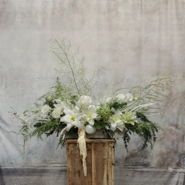 A winter floral arrangement with white amaryllis, casa blanca lilies, frosted evergreens, cascading amaranthus, and shimmering accents, ideal for holiday décor.