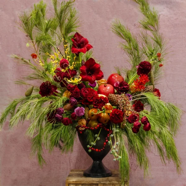 A grand arrangement with vermilion amaryllis, red roses, pomegranates, pinecones, and evergreen accents, part of the Celestial Yule Collection.