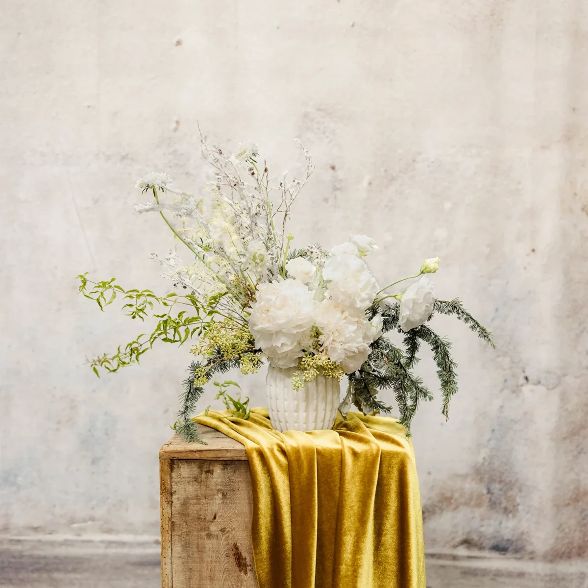 A winter arrangement with white blooms, frosted greenery, and airy accents in a textured vessel, perfect for holiday décor.