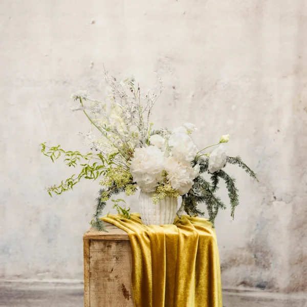 A winter arrangement with white blooms, frosted greenery, and airy accents in a textured vessel, perfect for holiday décor.