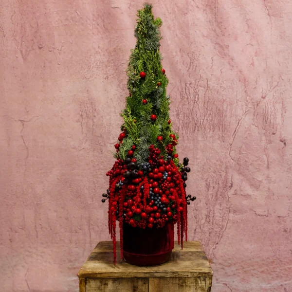 Holiday topiary featuring evergreen branches, vibrant red and black berries, cascading accents, and a velvet-covered base.