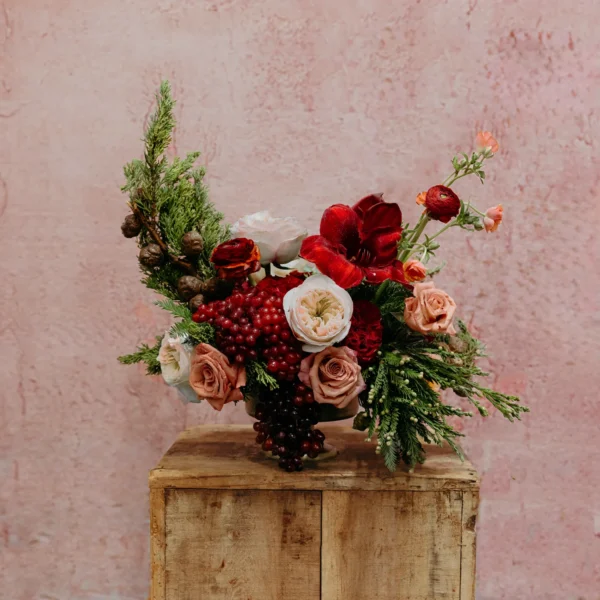 A festive arrangement featuring garnet amaryllis, peach and cream roses, red berries, and lush greenery, part of the Celestial Yule Collection.