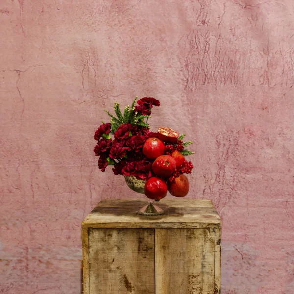 A bold arrangement featuring crimson carnations, fresh greenery, pomegranates, and berries, part of the Celestial Yule Collection.