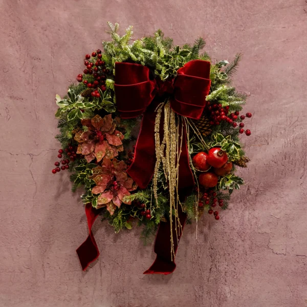 A festive wreath featuring evergreen branches, burgundy berries, shimmering poinsettias, pomegranates, and a velvet bow, part of the Celestial Yule Collection.