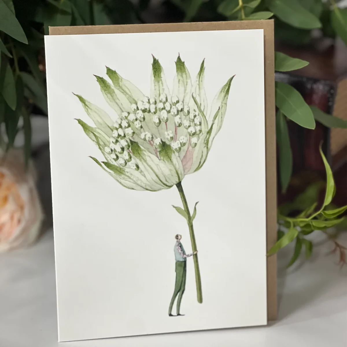 Illustrated card showing a tall white wildflower with green accents held by a small figure in green trousers and a patterned shirt.