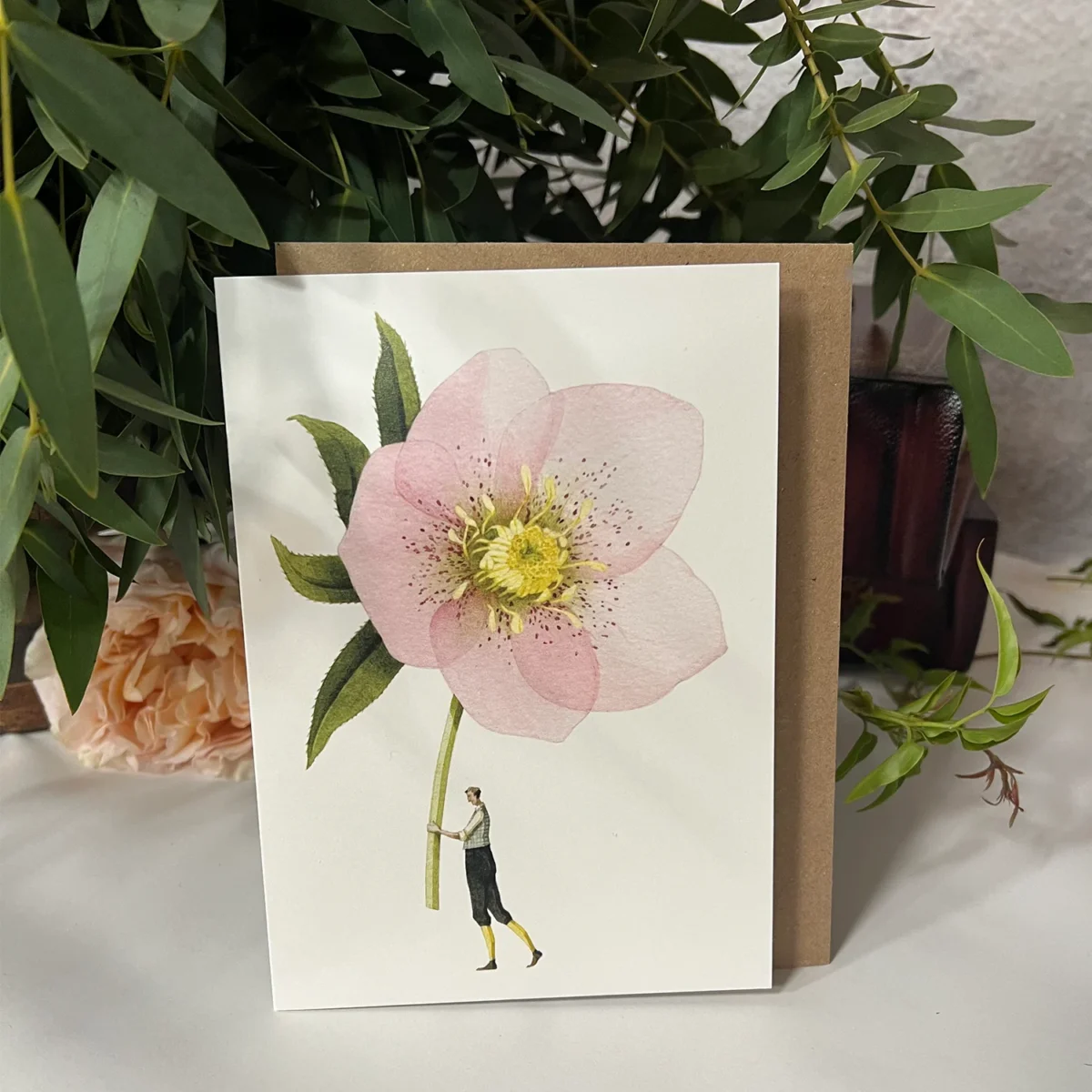 Greeting card featuring a large pink flower with yellow center, held by a small illustrated figure against a white background